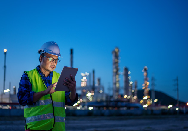 A man in a hard hat and vest is holding a tablet computer