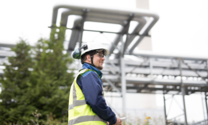 A man in a safety vest standing in front of a power plant
