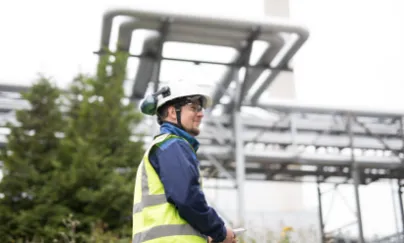 A man in a safety vest standing in front of a power plant