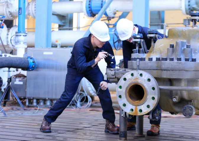 Two men in hard hats working on a large pipe