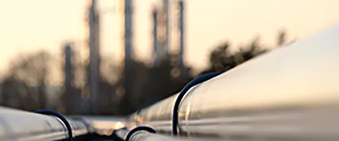 A close up of a pipeline with a large industrial plant in the background