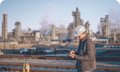 A man in a hard hat and jacket standing in front of an industrial plant