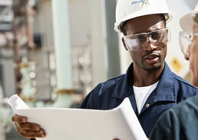 Two men in hard hats and safety glasses looking at a blueprint