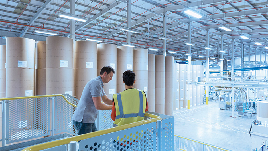 Two people standing in a warehouse with large rolls of paper