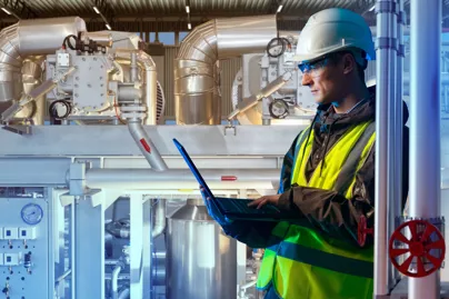 A man in a safety vest and hard hat using a laptop