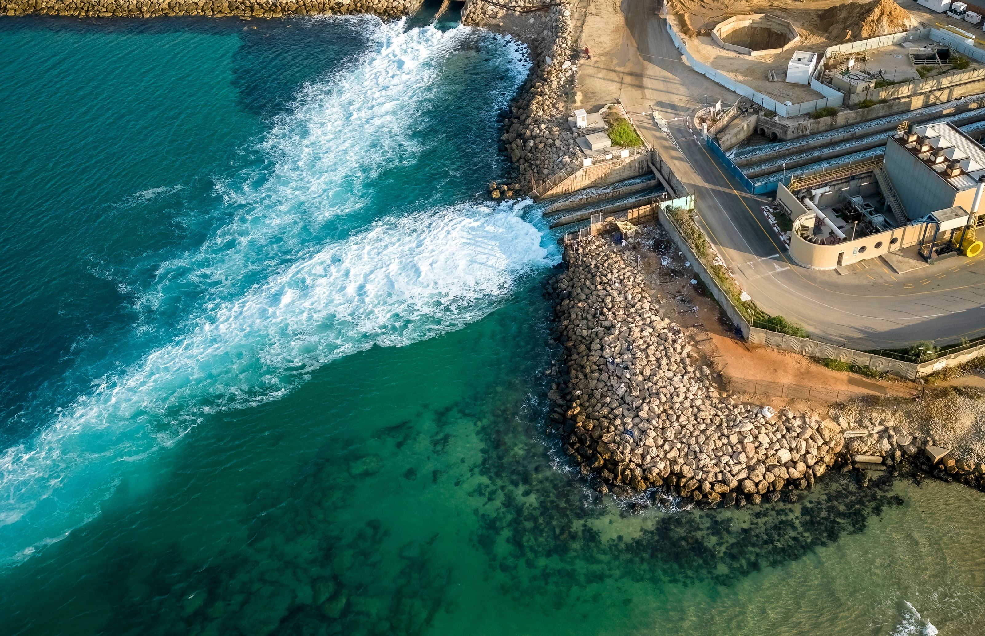 Aerial view of a coastal industrial facility with water discharge into the sea.