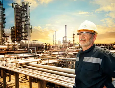 A man in a hard hat and safety glasses standing in front of an oil refinery