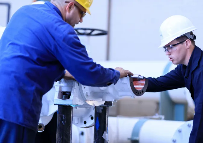 Two men in hard hats working on a pipe
