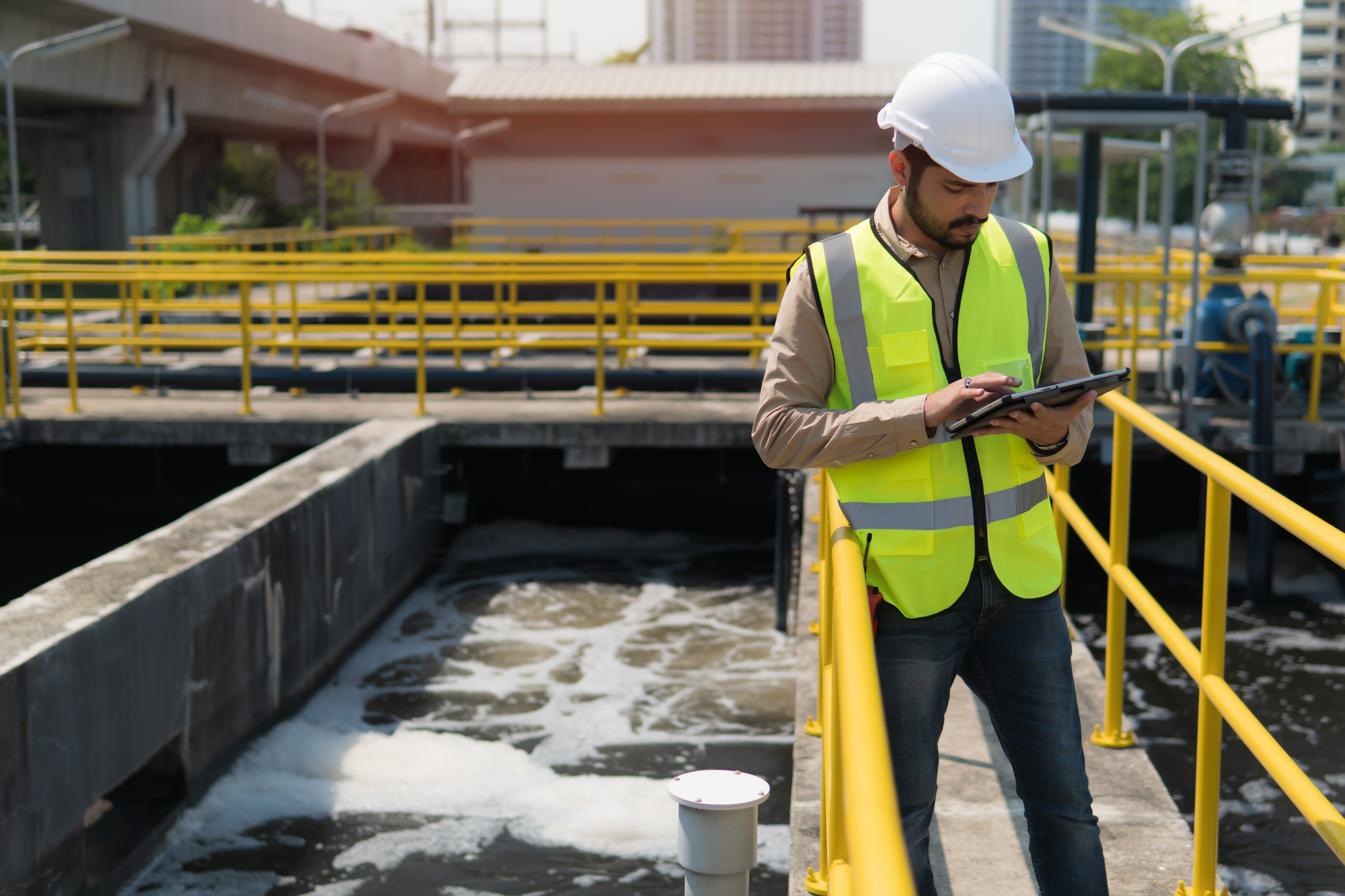 A man in a hard hat and vest standing on a bridge with a tablet