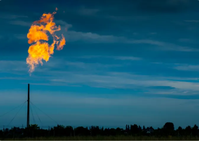 A gas flare illuminates the night sky, casting a bright glow against the dark night sky