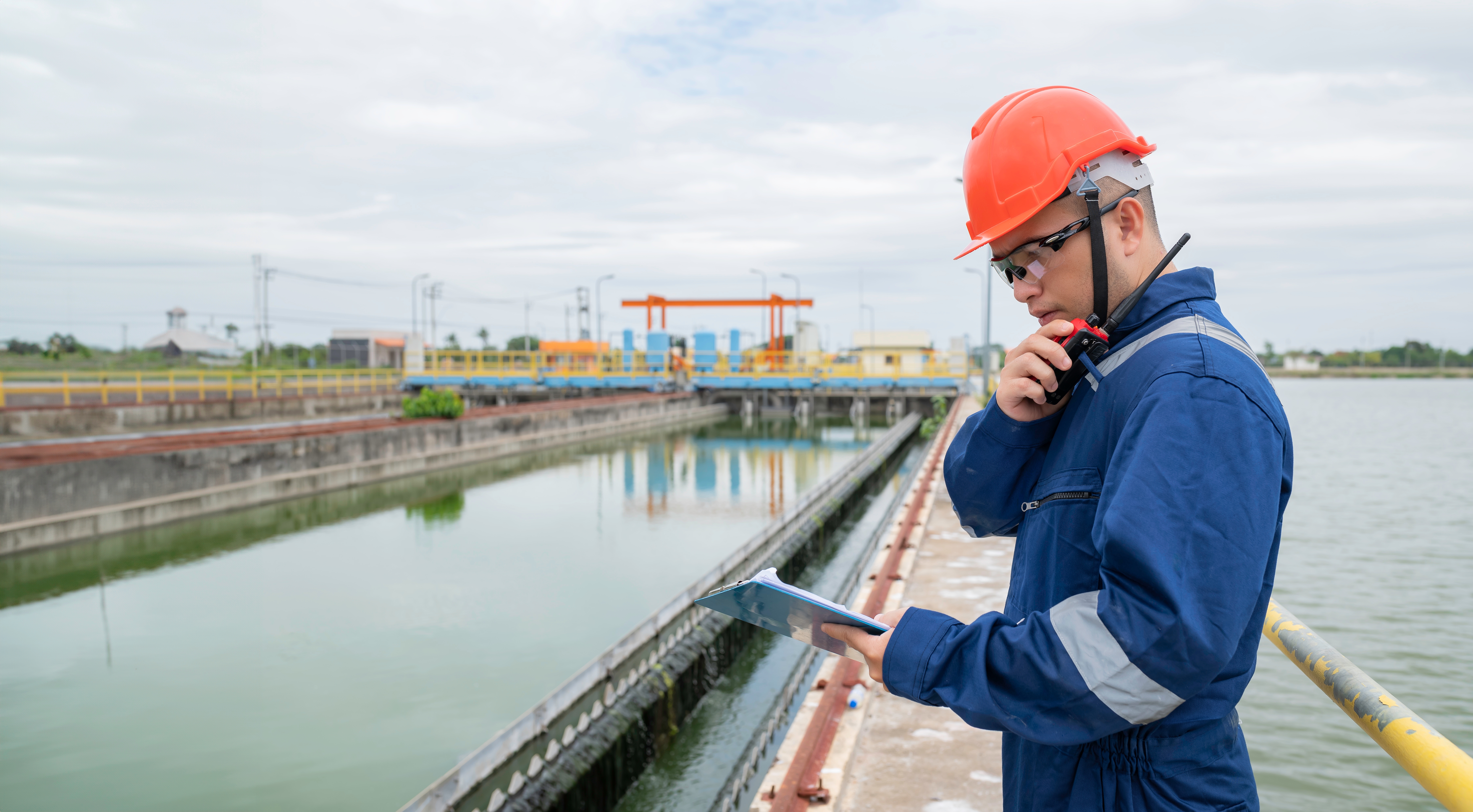 Engineer at a water treatment facility holding a clipboard and using a radio.