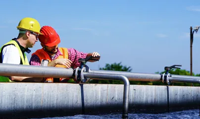 Two men in hard hats and safety vests working on a pipe