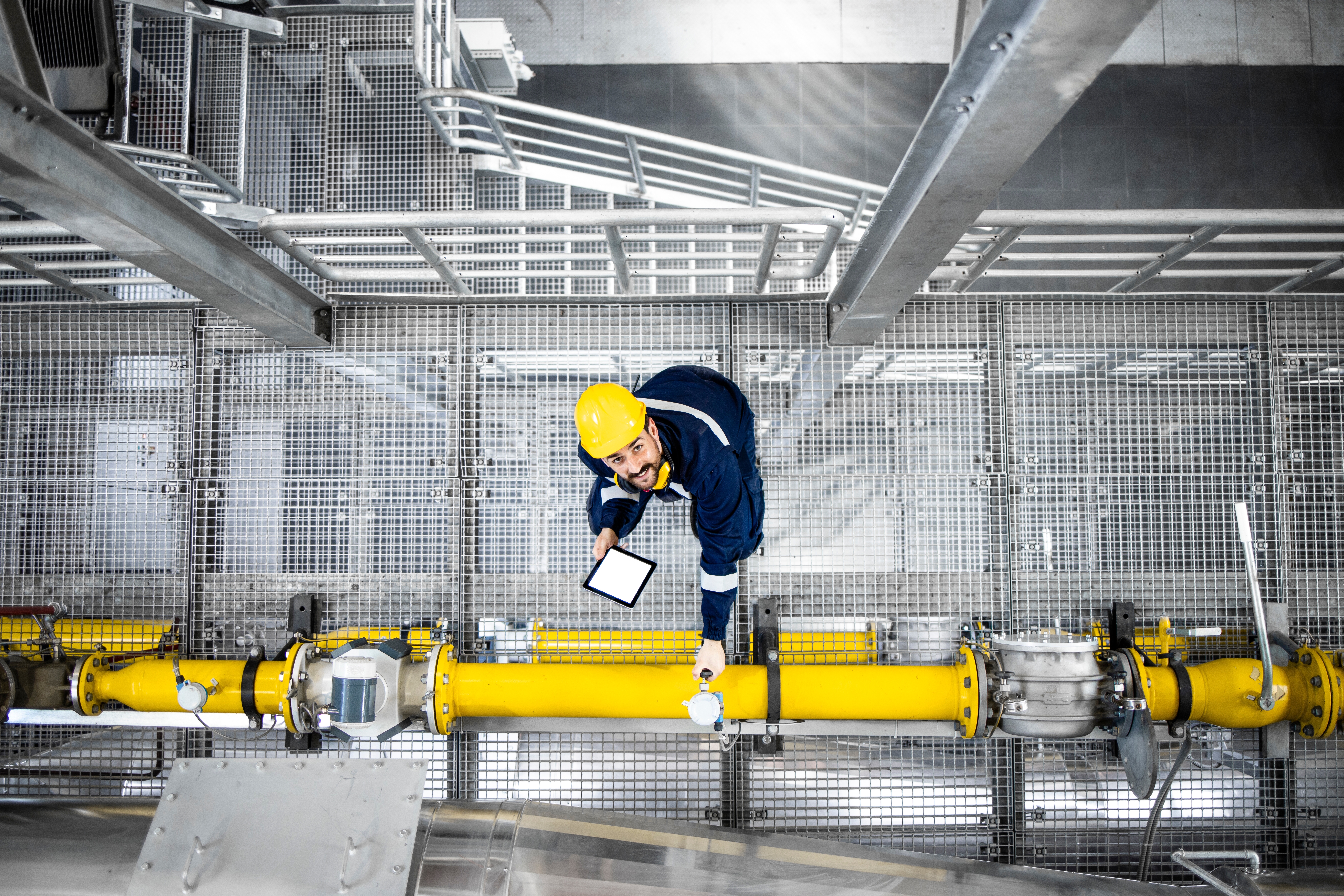 A man in a hard hat standing on mesh beside a yellow pipe