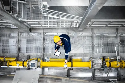 A man in a hard hat standing on mesh beside a yellow pipe