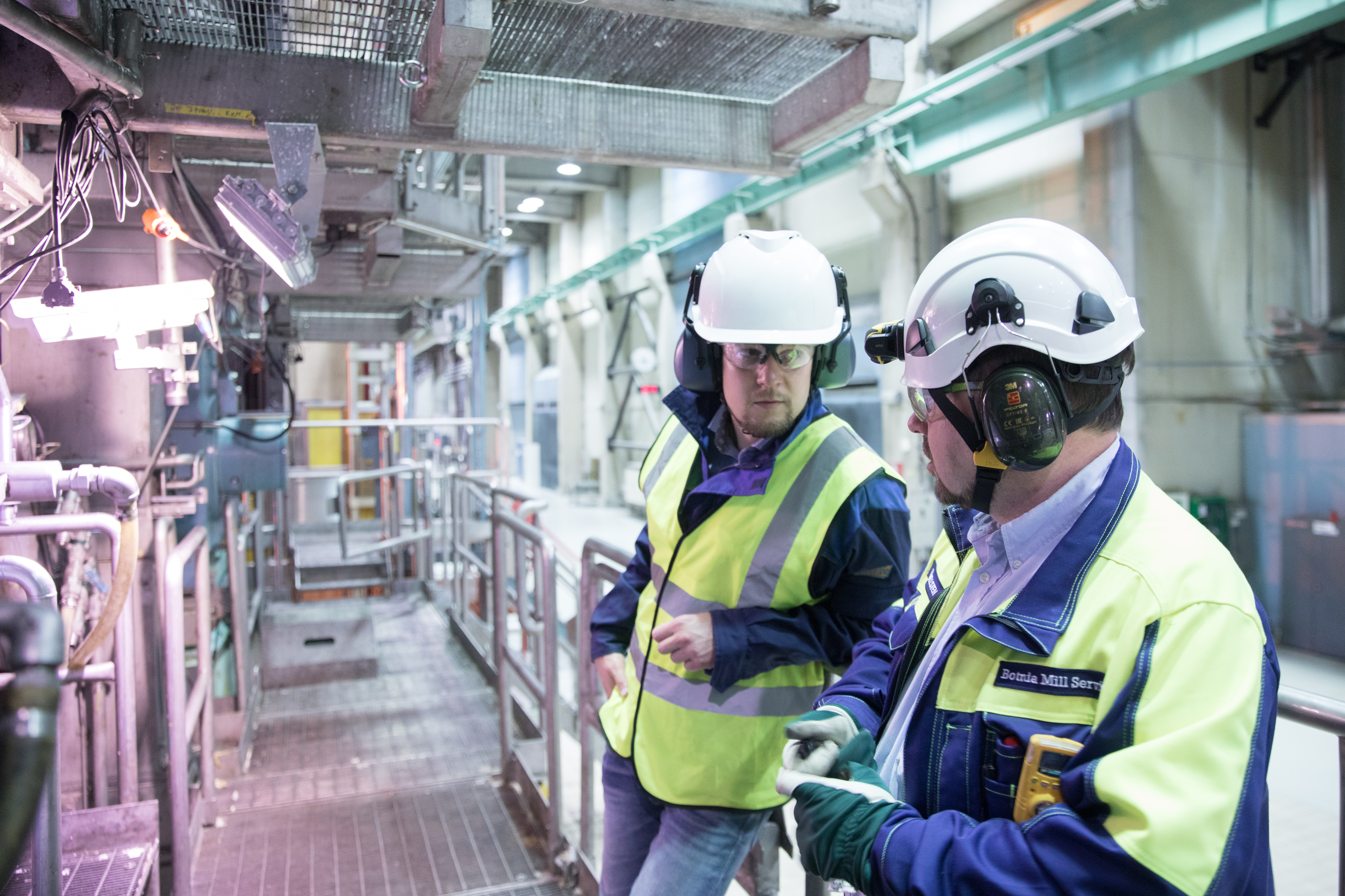 Two men in safety vests and hard hats standing in a factory