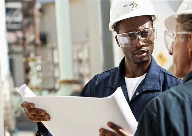 Two men in hard hats and safety glasses looking at a blueprint