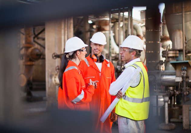 Three people in hard hats and safety vests talking to each other