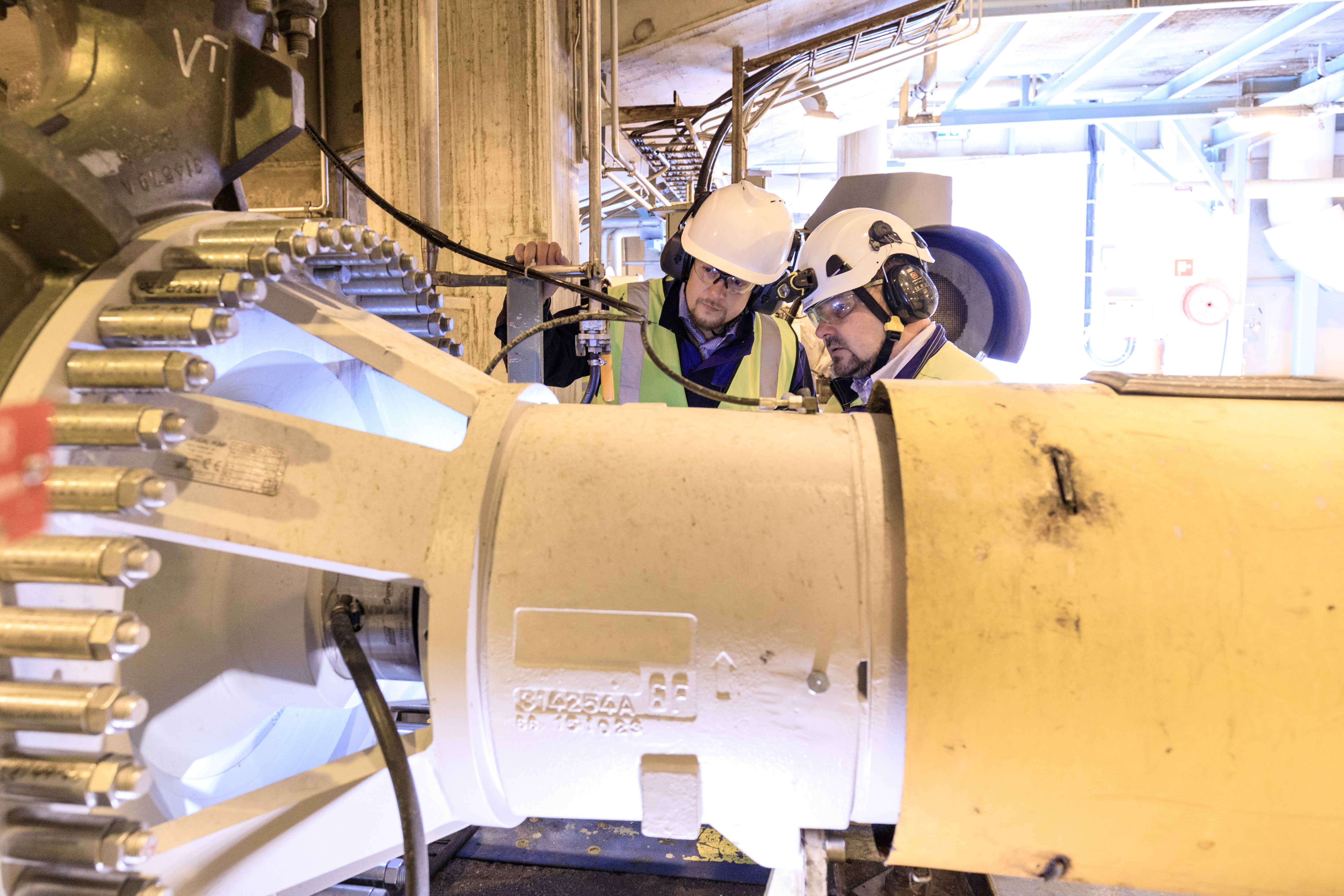 Two men in hard hats working on a large machine