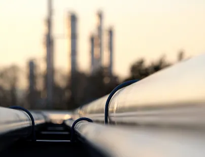 A close up of a pipeline with a large industrial plant in the background